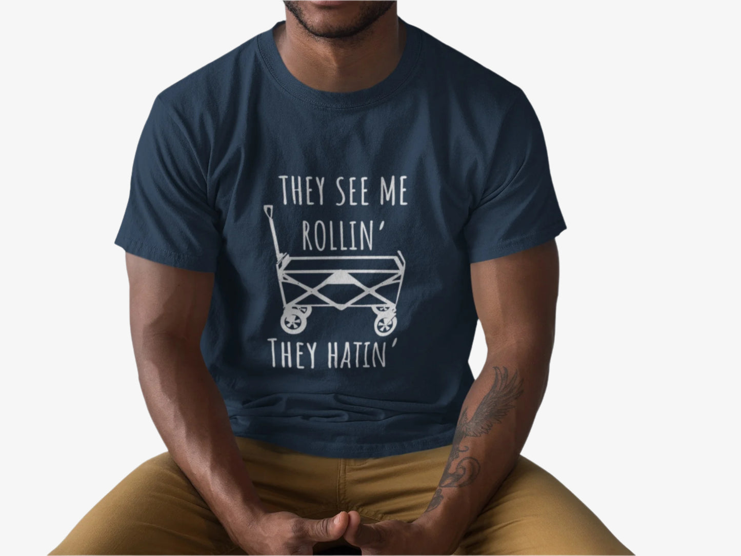 Person wearing a Navy blue t-shirt with white graphic playful design featuring a classic wagon graphic with the bold phrase, "They See Me Rollin' They Hatin'" on a white background