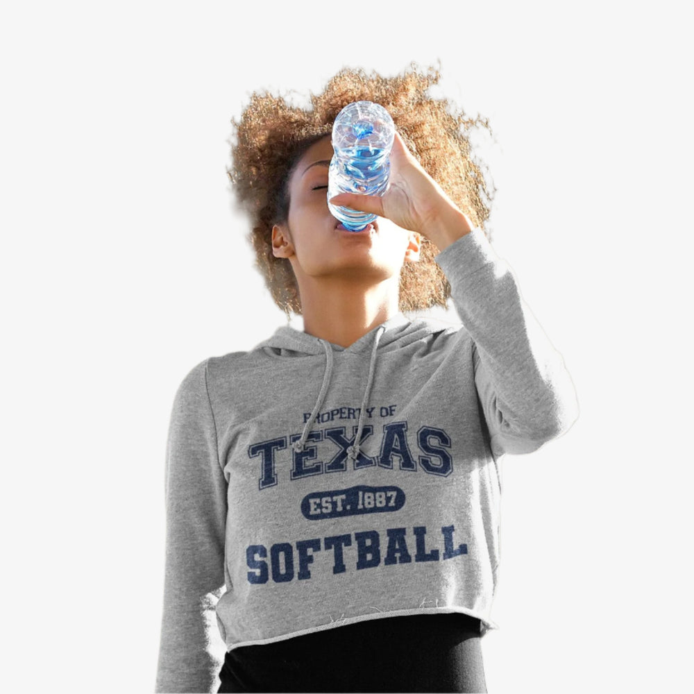 Person wearing a Gray hoodie with 'Property of Texas Softball' text drinking from a water bottle on white background.